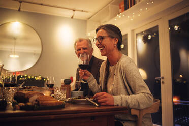 Älteres Paar genießt das Weihnachtsessen mit der Familie. Ältere Frau hält ein Glas Wein und spricht und lächelt am Esstisch. - JLPSF11132