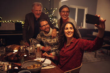 Eine Frau macht ein Selfie mit ihrer Familie an Heiligabend. Eine europäische Familie macht ein Selfie während des Weihnachtsessens; - JLPSF11138