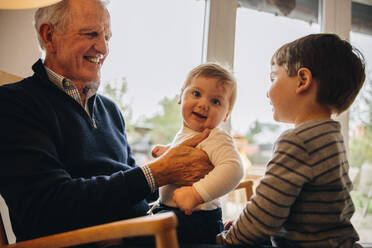 Ein Großvater, der sich mit seinen Enkeln zu Hause amüsiert. Die Kinder haben viel Spaß mit ihrem Großvater. - JLPSF11141