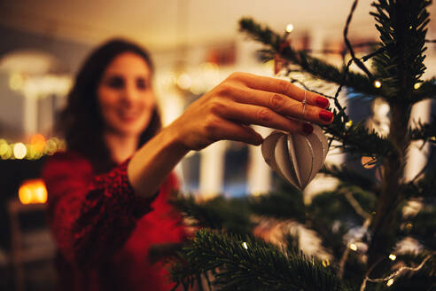 Nahaufnahme einer Frau beim Schmücken des Weihnachtsbaums. Hand einer Frau beim Binden von Schmuck am Weihnachtsbaum. - JLPSF11159