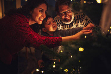 Small family decorating Christmas tree together. Parents with kid decorating at home. - JLPSF11160