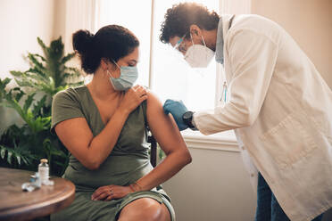 Doctor giving vaccine to woman at home. Female wearing face mask receiving covid-19 immunity vaccine from a healthcare professional at home. - JLPSF11171