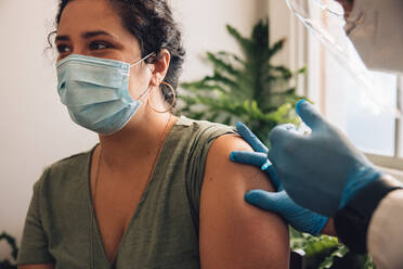 Nahaufnahme einer Frau mit Gesichtsmaske, die sich den Impfstoff gegen das Coronavirus in den Arm spritzen lässt. Eine Frau wird von medizinischem Personal zu Hause geimpft. - JLPSF11177