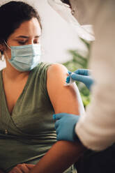 Woman getting vaccine at home. Healthcare professional cleaning and disinfecting female's arm before giving coronavirus vaccination shot at home. - JLPSF11216