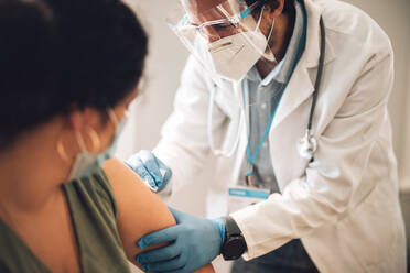 Arzt mit Gesichtsmaske und Schutzschild bei der Impfung einer Frau zu Hause. Frontline-Mitarbeiter verabreichen einer Frau zu Hause den Covid-Impfstoff. - JLPSF11220