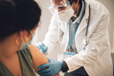 Doctor wearing face mask and shield vaccinating woman at home. Frontline workers giving covid vaccine to woman at her home. - JLPSF11220