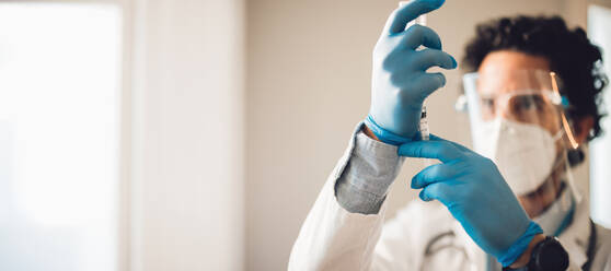 Hands of a frontline worker preparing vaccine syringe. Doctor making a vaccine injection ready for giving vaccination. - JLPSF11224