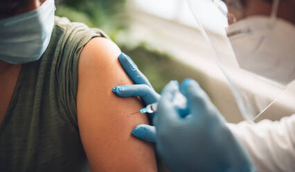 Closeup of a doctor vaccinating female at home. Healthcare professional giving covid-19 vaccine to a female at her home. - JLPSF11225