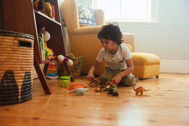 Niedlicher kleiner Junge, der mit buntem Tierspielzeug in seinem Spielbereich zu Hause spielt. Fantasievoller kleiner Junge, der auf dem Boden kniet und mit Dinosaurierspielzeug spielt. - JLPSF11237