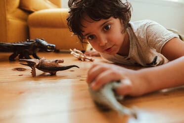 Little boy playing with his toys at home. Adorable young boy lying on the floor while playing with animal toys in his play area. - JLPSF11241