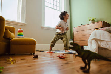 Verspielter Junge, der einen T-Rex-Dinosaurier nachahmt, während er zu Hause spielt. Kreativer kleiner Junge, der Spaß hat, während er in seinem Spielbereich steht. - JLPSF11243