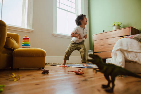 Playful young boy mimicking a t-rex dinosaur during playtime at home. Creative little boy having fun while standing in his play area. - JLPSF11243