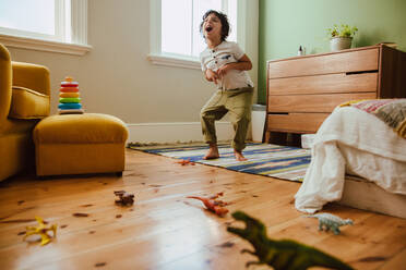 Kreativer kleiner Junge, der einen T-Rex-Dinosaurier nachahmt, während er in seinem Spielbereich zu Hause steht. Fantasievoller kleiner Junge, der Spaß beim Spielen hat. - JLPSF11244