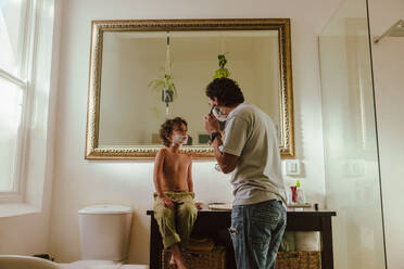 Father showing his son how to shave using shaving cream. Loving father teaching his son his shaving skills in the bathroom. Father and son spending some quality time together at home. - JLPSF11253