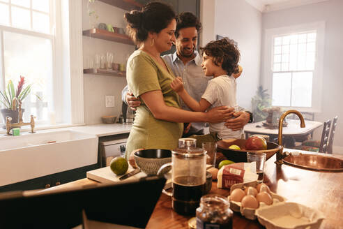 Liebevolle junge Familie lächelt glücklich, während sie sich in der Küche umarmen. Zwei liebevolle Eltern verbringen viel Zeit mit ihrem Sohn zu Hause. - JLPSF11276