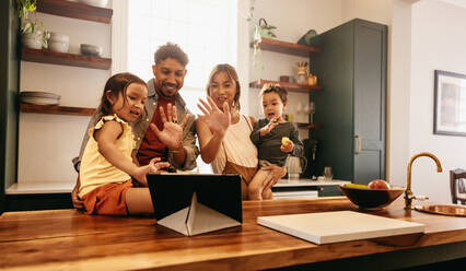 Eine glückliche Familie winkt während eines Videogesprächs mit ihren Lieben auf einem digitalen Tablet. Eine vierköpfige Familie lächelt fröhlich, während sie ihre Freunde und Familie online begrüßt. - JLPSF11308