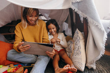 Supportive mother watching kids content with her daughter. Single mom smiling while sitting with her daughter in her play area. Mother and daughter spending some quality time at home. - JLPSF11317