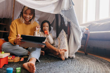 Cheerful mother and daughter watching kids content on a digital tablet. Single mom smiling while sitting with her daughter in her play area. Mother and daughter spending some quality time at home. - JLPSF11318