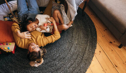 Overhead view of a mother and her daughter laughing happily at home. Cheerful mother and daughter lying on the floor in their play area. Mother and daughter spending some quality time together. - JLPSF11322