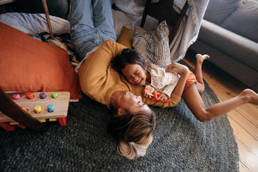 High angle view of a mother and her daughter laughing happily at home. Cheerful mother and daughter lying on the floor in their play area. Mother and daughter spending some quality time together. - JLPSF11323