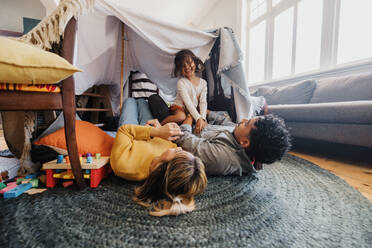 Junges Mädchen, das sich mit Mama und Papa auf dem Spielplatz vergnügt. Niedliches kleines Mädchen, das glücklich lächelt, während es auf seinem Vater sitzt. Eine dreiköpfige Familie, die eine schöne Zeit miteinander verbringt. - JLPSF11328