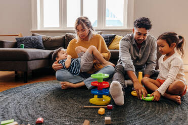 Mama und Papa spielen mit ihren Kindern im Wohnzimmer zu Hause. Zwei junge Eltern haben Spaß mit ihrem Sohn und ihrer Tochter während der Spielzeit. Eine vierköpfige Familie verbringt eine schöne Zeit miteinander. - JLPSF11335