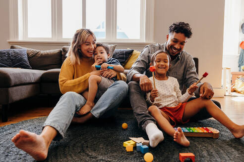 Liebevolle Eltern, die mit ihrem Sohn und ihrer Tochter im Wohnzimmer spielen. Mama und Papa haben Spaß mit ihren Kindern beim Spielen. Eine vierköpfige Familie verbringt eine schöne Zeit zu Hause. - JLPSF11338