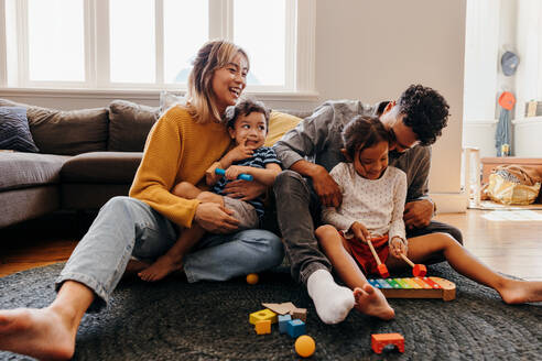Junge Eltern spielen mit ihrem Sohn und ihrer Tochter im Wohnzimmer. Mutter und Vater haben Spaß mit ihren Kindern beim Spielen. Eine vierköpfige Familie verbringt eine schöne Zeit zu Hause. - JLPSF11339