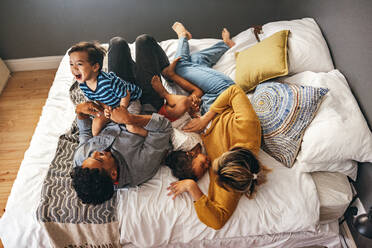 Overhead view of parents playing with their children on a bed. Happy family laughing and having fun together on the weekend. Mom and dad spending some quality time with their children. - JLPSF11342