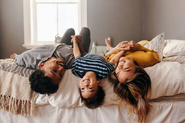 Happy family laughing and having fun together in their bedroom. Two ethnic parents playing with their son on the weekend. Mom and dad spending some quality time with their young son. - JLPSF11344