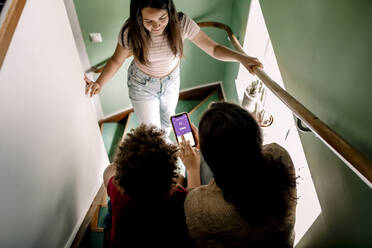 Mutter verwendet Hausautomatisierungs-App auf Smartphone mit Sohn und Tochter im Treppenhaus - MASF31972