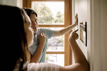 Mother and daughter using home automation through digital tablet mounted on wall at home - MASF31978