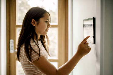 Seitenansicht eines Mädchens, das die Hausautomatisierung über einen an der Wand montierten Tablet-PC nutzt - MASF31987