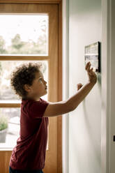 Side view of boy using home automation through tablet PC mounted on wall - MASF31993