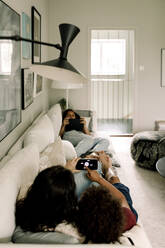 Familie nutzt drahtlose Technologien, während sie zu Hause auf dem Sofa liegt - MASF31998