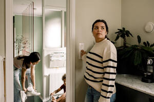 Frau, die den Lichtschalter ausschaltet, während sie zu Hause in der Nähe der Eingangstür steht - MASF32001