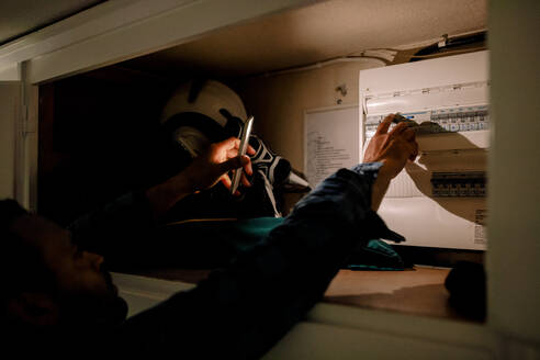 Mann, der während eines Stromausfalls mit der Taschenlampe seines Smartphones einen Schalter am Sicherungskasten einschaltet - MASF32011