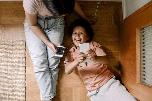 Direkt über der Aufnahme von glücklichen Geschwistern, die Smartphones auf dem Parkettboden zu Hause benutzen - MASF32017