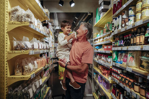 Lächelnder älterer Mann mit Enkel beim Einkaufen von Snacks im Supermarkt - MASF32030