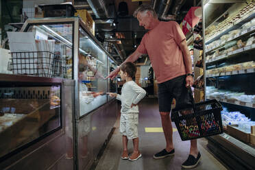 Älterer Mann zeigt seinem Enkel beim Einkaufen im Supermarkt Lebensmittel in der Auslage - MASF32031