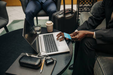 Junge Geschäftsfrau hält eine Kreditkarte in der Hand und benutzt einen Laptop in einer Hotel-Lounge - MASF32081