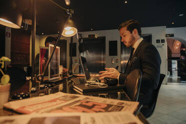 Junger Geschäftsmann mit Laptop sitzt am Schreibtisch im Büro - MASF32102