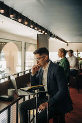 Businessman with hand on chin looking at laptop in hotel - MASF32116