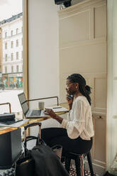 Seitenansicht eines weiblichen Berufstätigen, der am Schreibtisch im Büro sitzt und mit dem Handy telefoniert - MASF32154