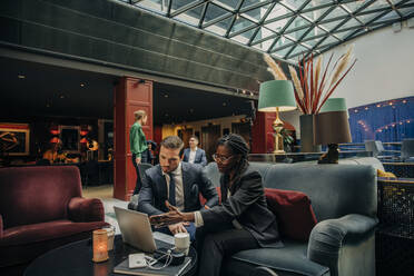 Young businesswoman discussing over laptop with male colleague in hotel lounge - MASF32185