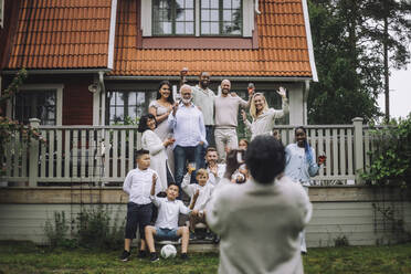 Frau fotografiert fröhliche Mehrgenerationenfamilie auf der Veranda vor dem Haus - MASF32221