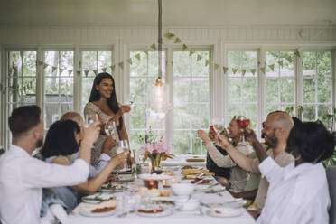 Smiling woman toasting drink with family members during dinner party at home - MASF32242