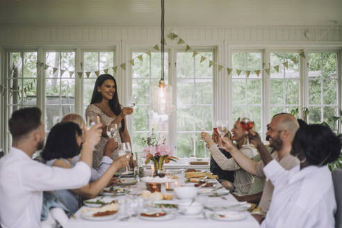 Lächelnde Frau stößt mit Familienmitgliedern auf ein Getränk während einer Dinnerparty zu Hause an - MASF32242