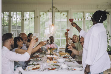 Frau stößt mit ihrer Mehrgenerationenfamilie am Esstisch während einer Dinnerparty zu Hause an - MASF32243