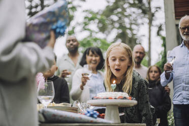 Glückliches Mädchen, das während einer Geburtstagsfeier mit seiner Familie eine Kerze auf dem Kuchen ausbläst - MASF32257